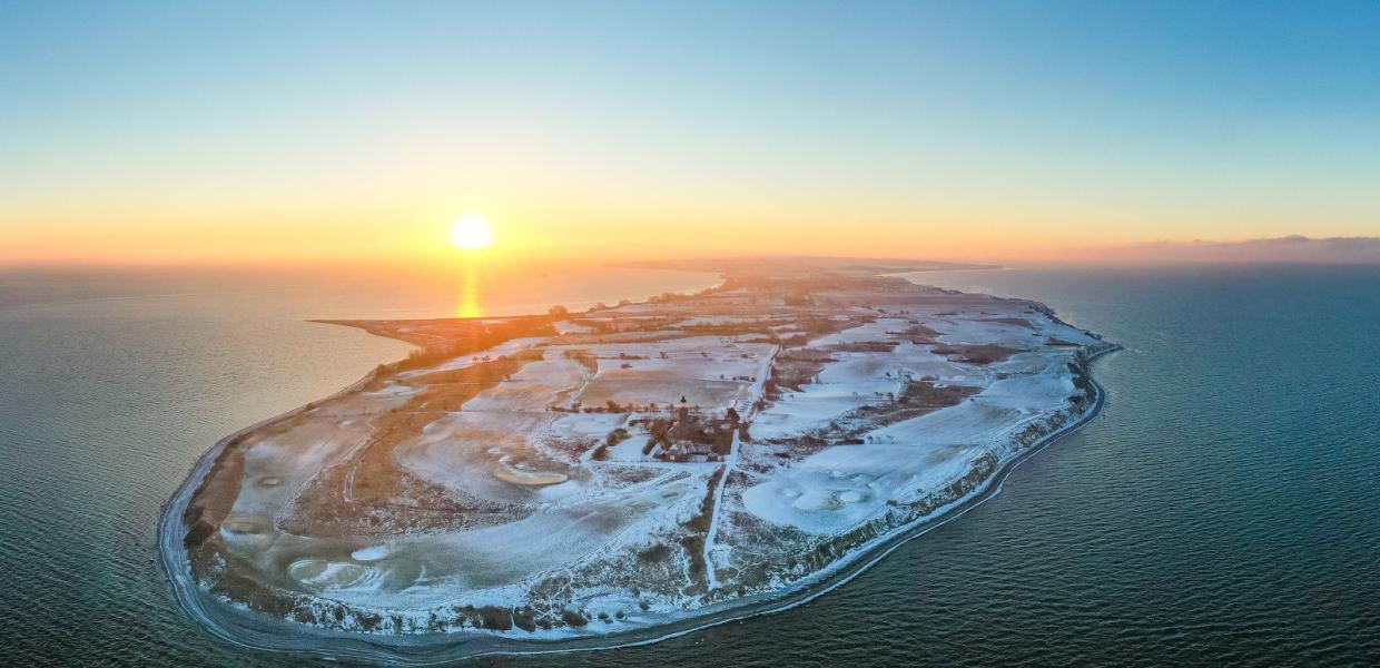 Luftfoto af Vestærø, fyr og golfbane med sne og solnedgang